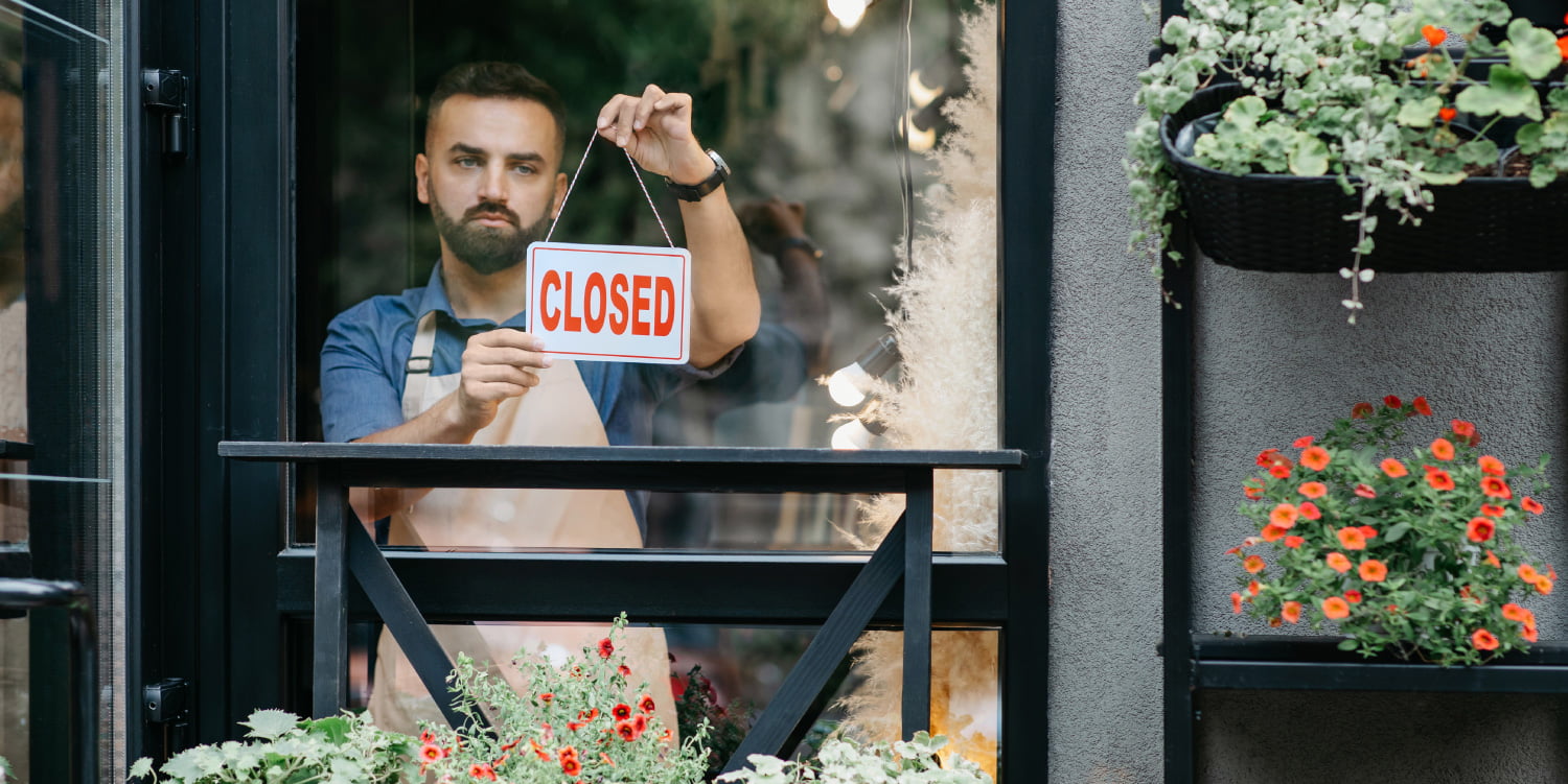 Caucasian man in apron closing his shop with a closed sign