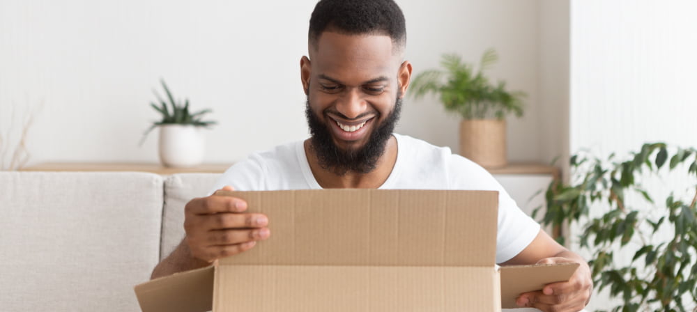 Man with beard and short hair opening a cardboard box and smiling