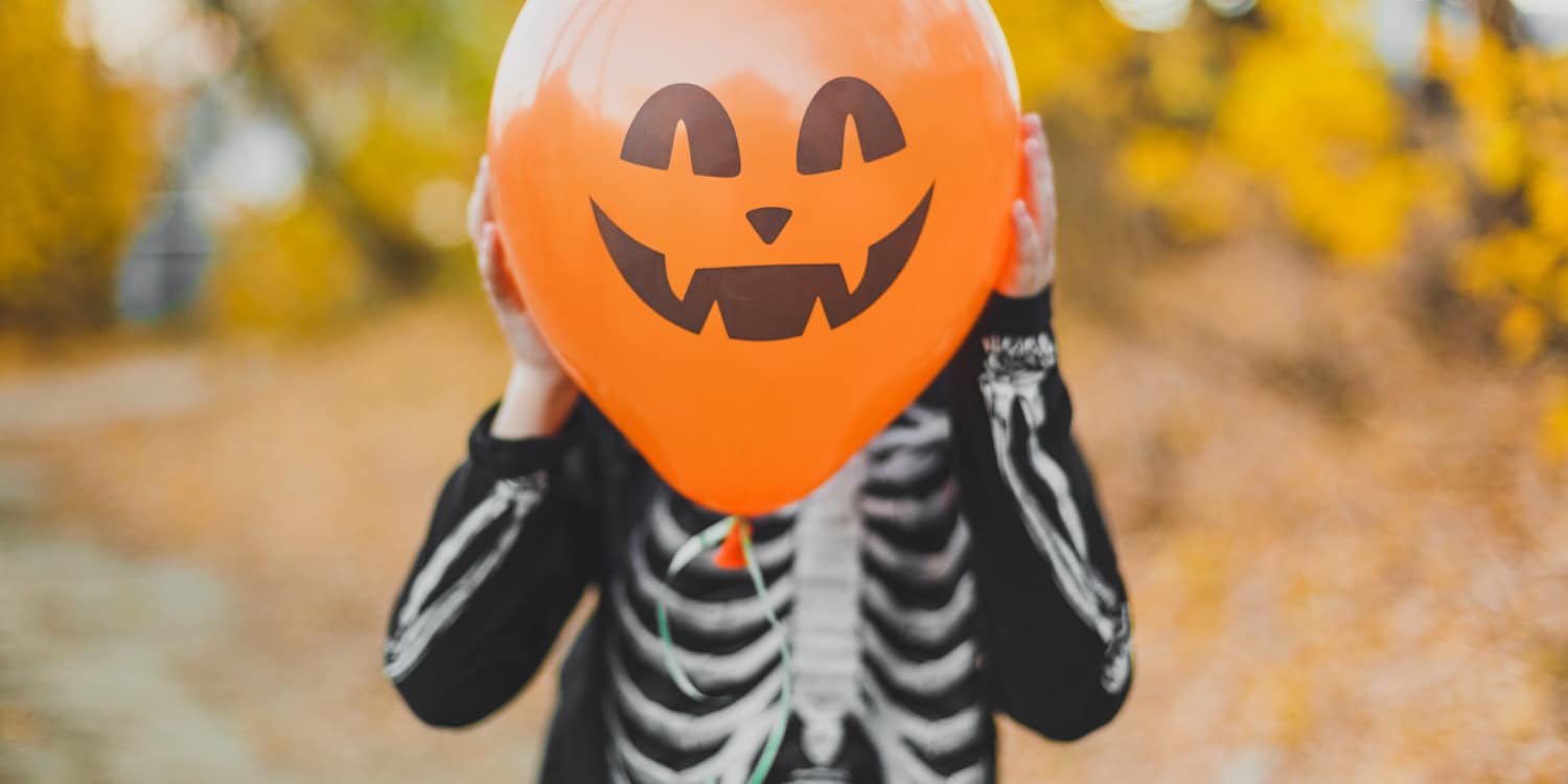 Child playing with pumpkin and skeleton outfit, holdin the pumpkin up to his head for Halloween sales